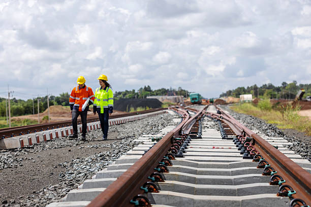 istock Two railway engineers wearing helmets and reflective jackets walk along new rail tracks under construction. The image represents teamwork, infrastructure development, and modern railway engineering. 2241144214