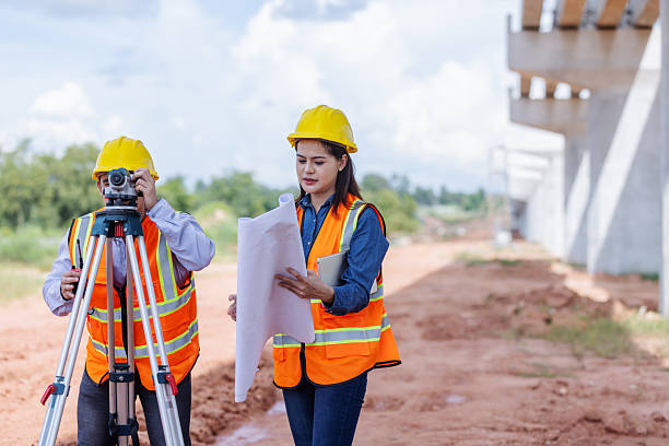 istock Two civil engineers wearing helmets and reflective vests survey a bridge construction site using a tripod instrument and blueprints. 2241145122