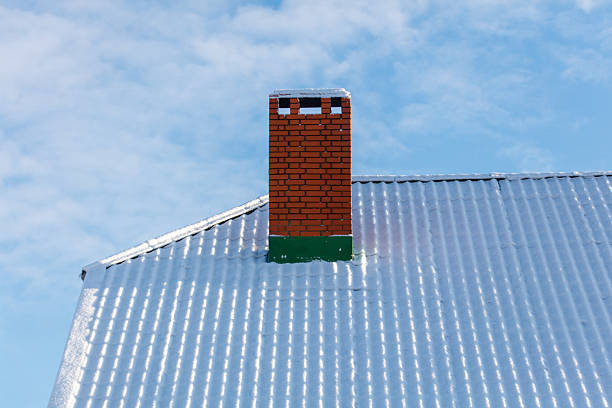 A chimney on a roof with snow on it. The chimney is red and has a green trim