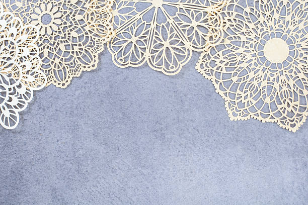 Row of lace doilies are arranged in a row on a gray surface. The doilies are of various sizes and shapes, and they create a sense of elegance and sophistication. Scene is one of refinement
