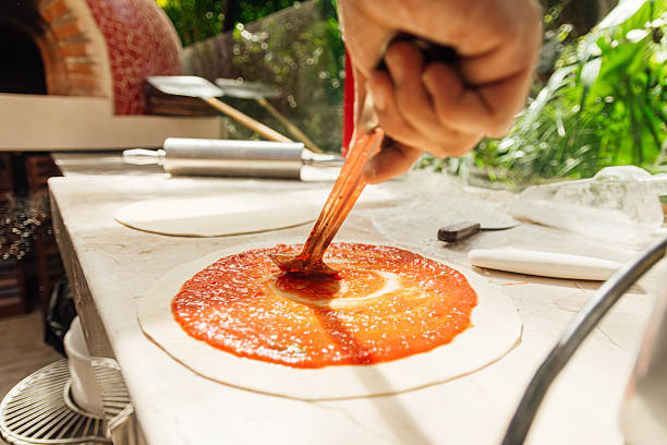 istock Spreading fresh tomato sauce on pizza dough by hand 2241149908