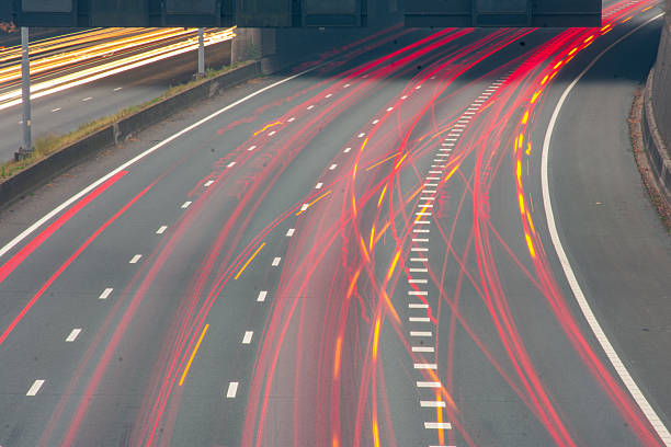 Dynamic long exposure photograph of highway traffic showing red and yellow light trails curving through empty lanes. The lines of motion symbolize speed, energy, and modern transportation. Great for illustrating motion, technology, infrastructure, or the pace of urban life.