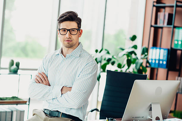 istock Confident young businessman standing with arms crossed in a modern bright office emphasizing professional success and leadership 2241153928