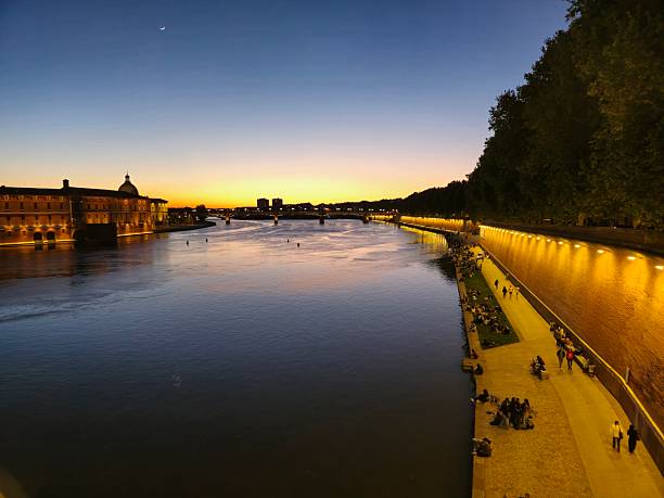 Toulouse is the 4th largest city in france,  its metropolitan area has a population of 1.5 million inhabitants. The image shows the garonne river and some people around during sunset.