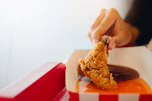 istock Fried chicken concept. Hand Holding Crispy Fried Chicken Piece with Sauce Served in a Red and White Tray at a Food Establishment 2241156829