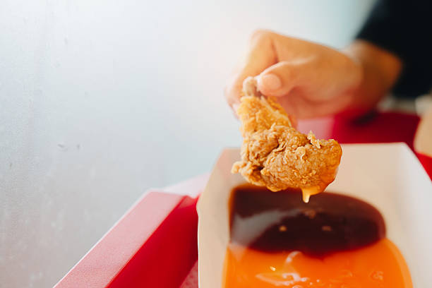 istock Fried chicken concept. Crispy fried chicken wing held by hand above rich sauce in takeout container with vibrant colors and modern setting 2241157008