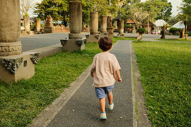 Toddler walking paved path in a park with stone pillars, exploring the outdoors from behind during childhood