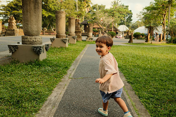 Boy playing outdoors on a path, looking back and smiling. Stone columns and green trees providing a natural setting