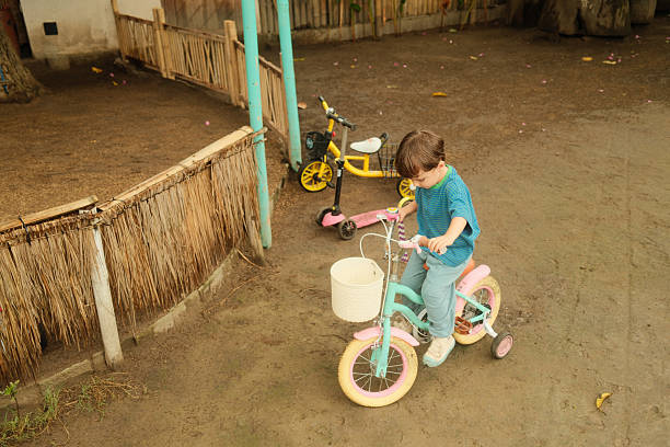 Child practices riding a colorful bicycle with training wheels on a dirt path, enjoying outdoor play in childhood