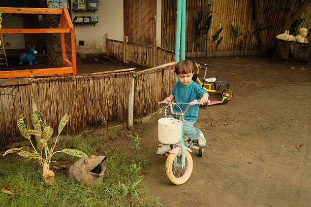 Young child pedaling a tricycle with a basket in a simple outdoor setting, enjoying playtime on a dirt path