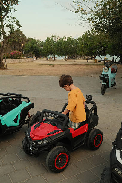 Young child experiencing happy outdoor playtime, sitting in a red toy car at a park near the beach during evening
