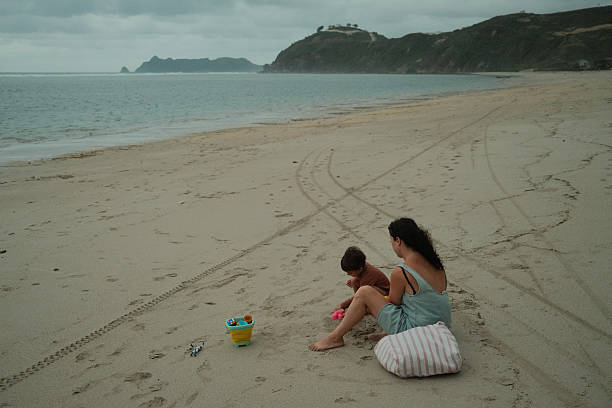 Mother and young child enjoying quality time together, playing with toy bucket and tools on a sandy beach