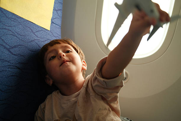 Young boy smiles while holding a toy airplane up to the window during an airplane journey, imagining flying