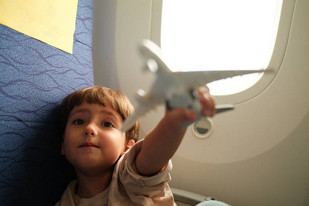 Young child in airplane seat holding toy plane to window, smiling with vivid imagination during flight, dreaming of adventure and travel
