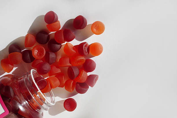 istock Red and orange gummy vitamins spill from a transparent bottle onto a white surface 2241160432