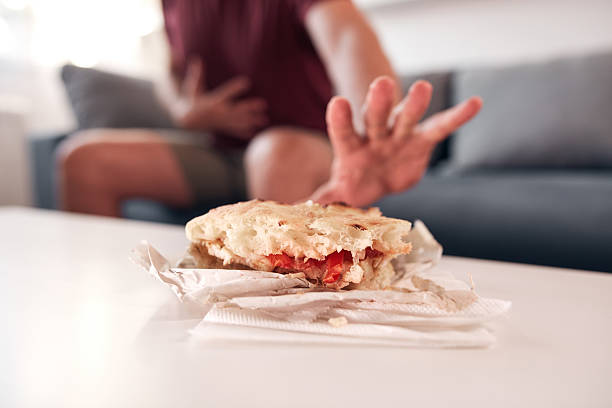 Smiling young woman holding a delicious sandwich filled with ham and fresh arugula, savoring a quick and healthy lunch in her cozy kitchen at home. Enjoying every bite