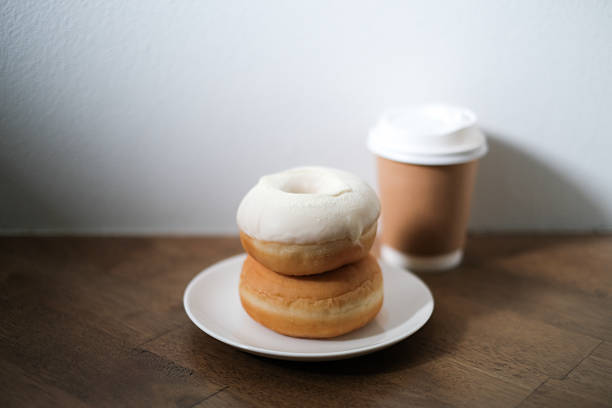 Breakfast donut in white plate and hot coffee on wooden table.
