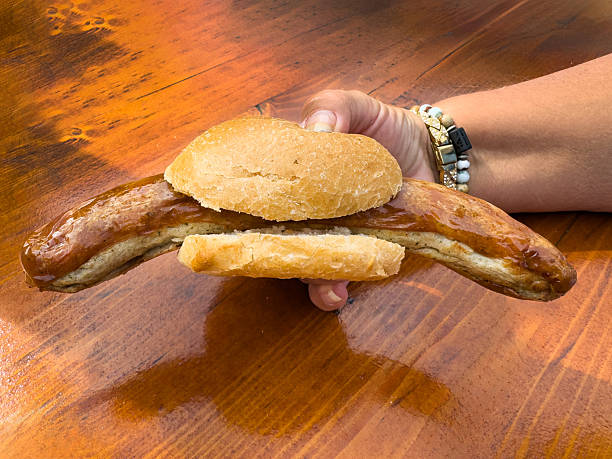Grilled German bratwurst sausage in a bread bun held in a hand