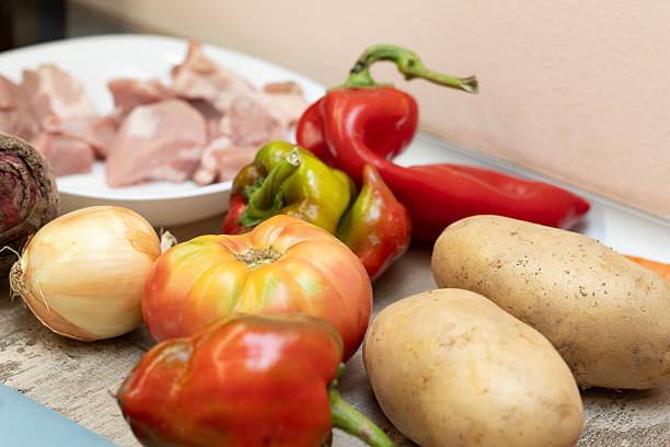 Close-up of fresh raw meat and veggies (tomatoes, onions, peppers, potatoes, beetroot) on wood, ready for a healthy home-cooked meal.