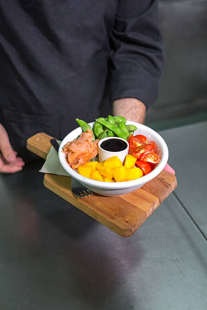 Unrecognizable chef showing fresh colorful poke bowl with salmon on restaurant kitchen