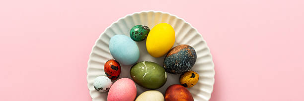 istock A collection of vibrant Easter eggs in various colors is artfully arranged on a white plate, set against a soft pink background, capturing the essence of the holiday's decorations, banner 2241175051