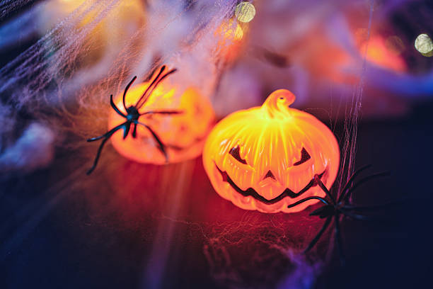 Glowing jack-o'-lantern decorations paired with black spiders and cobwebs in a soft, warm light. The composition captures the fun and mysterious mood of Halloween night. Copy space for text - Halloween, holiday