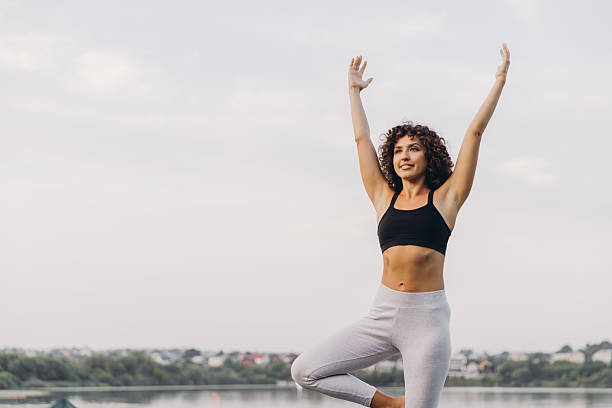 istock Young woman practicing yoga tree pose by the lake 2241175874