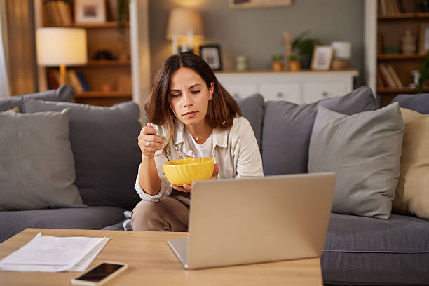 istock Young woman eating breakfast while using laptop at home 2241176801