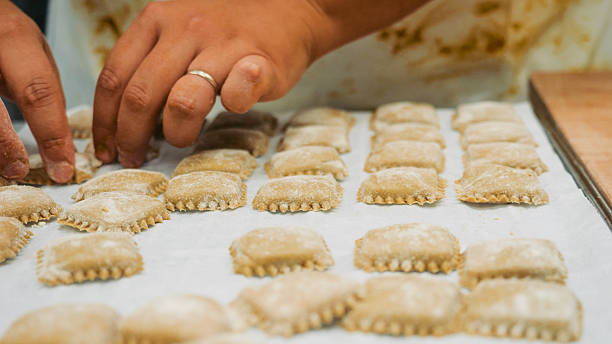 istock Closeup of hands carefully arranging rows of freshly made uncooked ravioli on a parchment paper lined baking sheet ready for cooking preparation food making process 2241183607