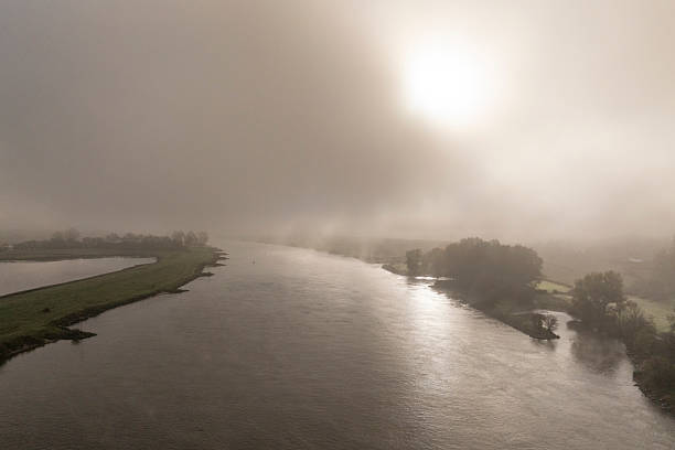 IJssel river meandering through the landscape during a foggy autumn morning near Zwolle and Hattem seen from above.