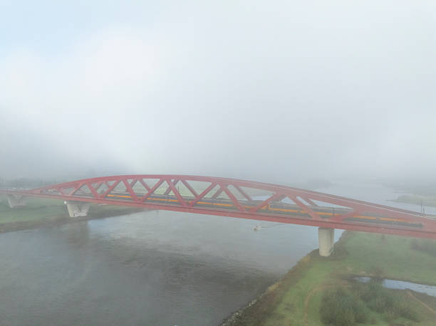 Hanzeboog train bridge over the river IJssel with during a foggy autumn morning and a train of the NS passing over the red bridge near the city of Zwolle in Overijssel, The Netherlands. Aerial drone point of view.