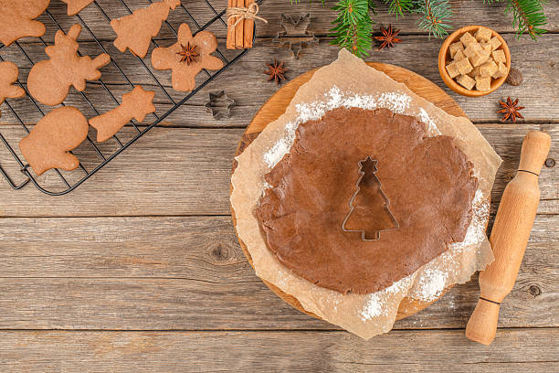 istock Christmas baking concept with gingerbread dough, cookie cutter in tree shape, and festive cookies on a rustic wooden background. copy space. top view 2241190359