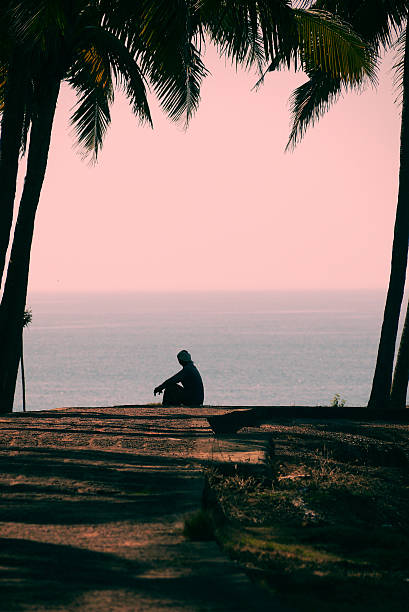 isolated man looking at dramatic sunrise sky over sea horizon from rocky shore