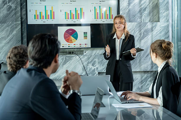 istock Female business presenter standing front digital board leading strategy meeting with multiracial colleagues listening analyzing financial data during team collaboration corporate session 2241196683