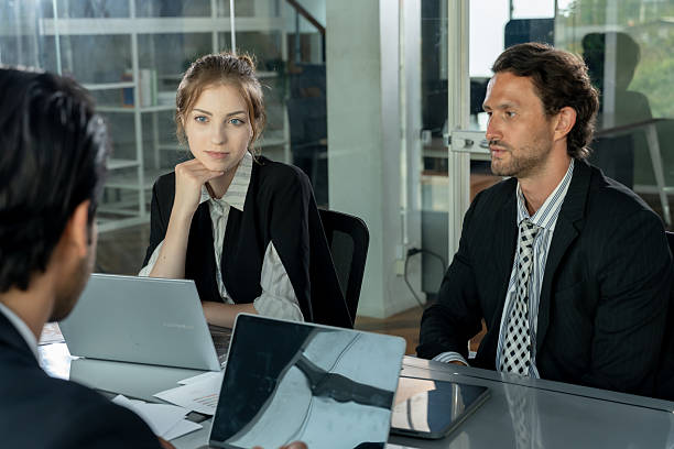 istock Multiracial business executives sitting at meeting table with laptops and documents discussing reports while caucasian female listening attentively during collaboration in office 2241196713