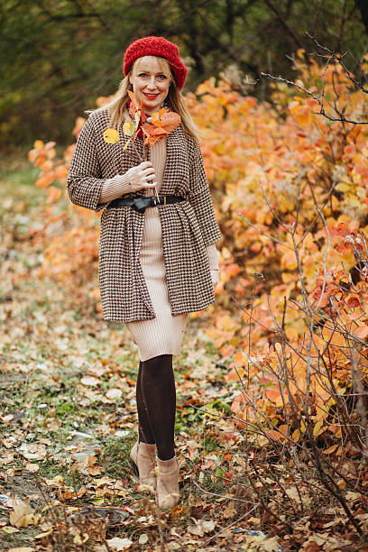 A mother and daughter wearing matching red hats enjoy a peaceful walk through a colorful autumn forest, holding hands and gathering leaves among golden and orange shrubs, capturing warmth, connection, and cozy fall vibes.
