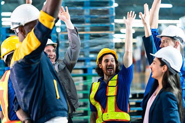 istock Multiracial warehouse employees celebrating teamwork success raising hands together in cheerful mood wearing safety uniform and helmet inside storage facility with industrial background 2241203761