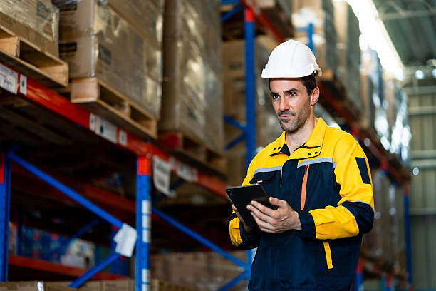 istock caucasian warehouse inspector wearing safety uniform and hardhat checking inventory record using tablet device while walking through shelves inside large storage center for supply control 2241203798