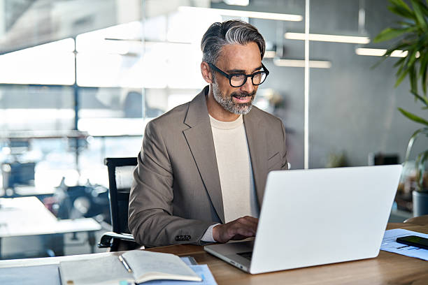 istock Smiling middle aged business man executive sitting at desk using laptop. 2241204390