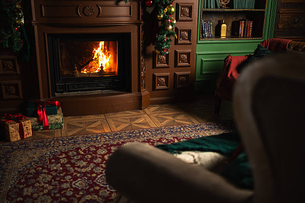 Cozy, luxurious, and white modern living room with a modern white fireplace in the middle of two high, large windows with a nice winter idyllic view (snow, trees) and elegant curtains on the carpet floor. \nA few wrapped gifts under the green and golden Christmas-decorated tree in front of the window and a blank white plaster wall background with copy space.  A slight close-up of the fireplace and the Christmas tree. A slight vintage effect was added. 3D rendered image.