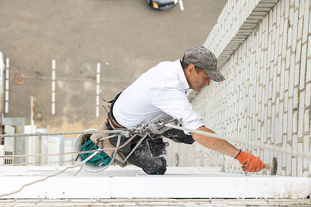 Construction worker insulating the building facade at the height of the ninth floor. The worker is hanging on climbing ropes outside the building, securing polystyrene panels to the brick wall using plastic construction anchors.