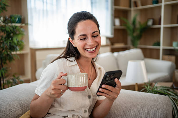 istock Happy woman using phone holding mug on couch 2241212261
