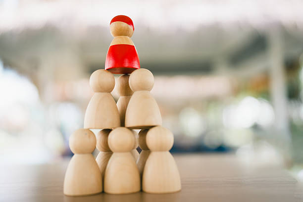 Wooden figures stacked in pyramid structure with red leader on top, symbolizing leadership, teamwork, hierarchy, business management, and organizational success in team collaboration.