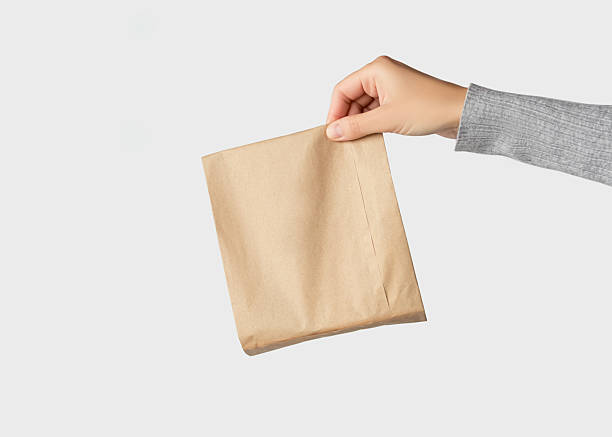 istock Hand holding a small brown paper package on a white background 2241216876