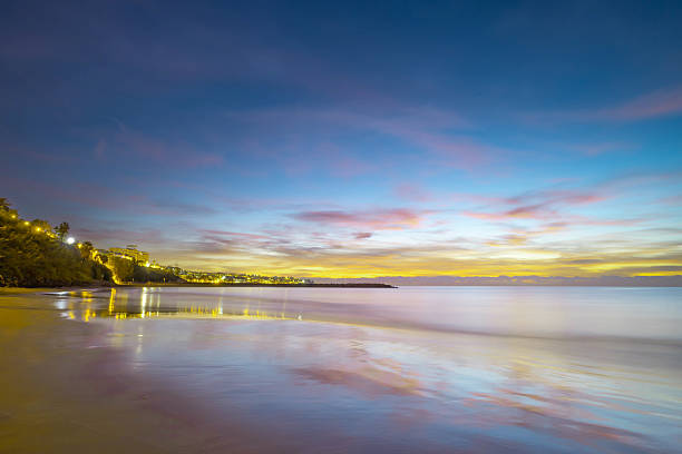 A vibrant sunrise lights up the sky over the beaches of Gran Canaria, with warm golden tones reflecting on the calm ocean and soft sand. A peaceful early morning seascape.