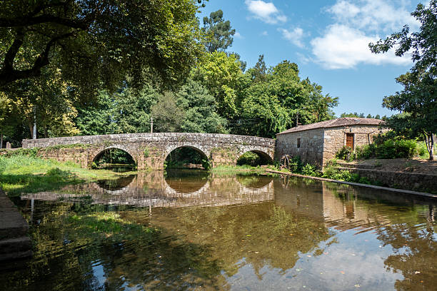 Historic stone bridge and watermill in Estorãos in Ponte de Lima with the reflection of the centuries-old structures and lush vegetation in the calm waters of the river