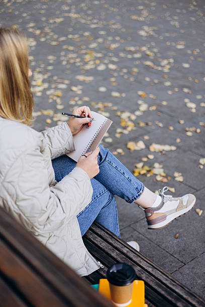 istock Young woman writing in notebook on bench in autumn park. 2241229691