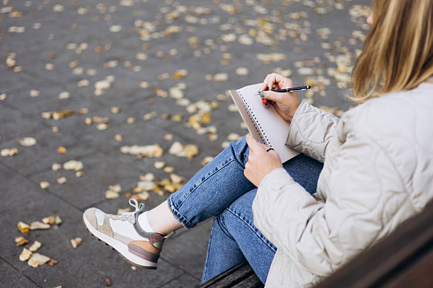 istock Young woman writing in notebook on bench in autumn park. 2241229693