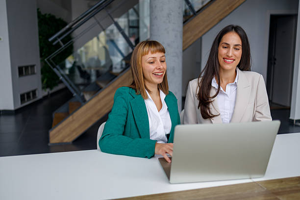 istock Two businesswomen collaborating on laptop, working together in modern office, smiling while planning project 2241231566