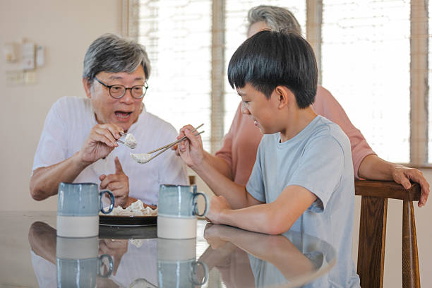 istock A curious Chinese boy tries to master chopsticks, clumsily picking up dumplings while his grandparents watch fondly in the kitchen. 2241231660
